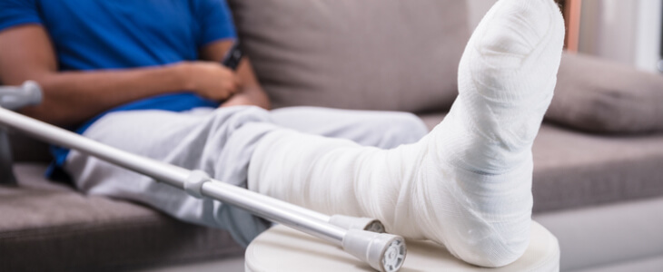 Man sitting on the couch while lifting his injured leg from a broken bone injury