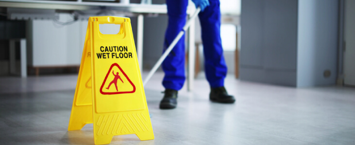 Janitor mopping up floors in a corporate office with a "Caution" sign to prevent a slip and fall accident