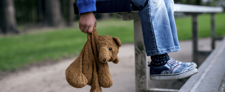 Minor holding a teddy bear alone on a bench.